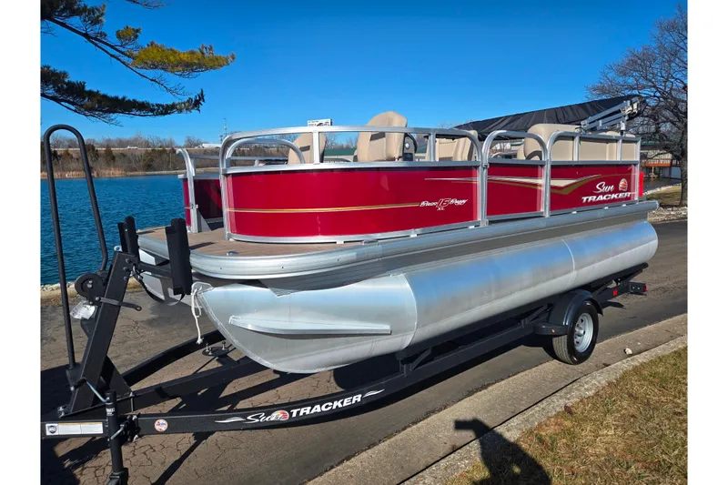 Slide: The Image of 2024 Sun Tracker Bass Buggy 16 XL Select pontoon boat on trailer by a lake. - 8