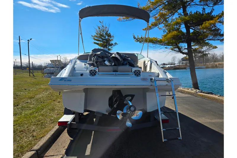 Slide: The Image of 2020 Crownline Eclipse E235 boat with ladder, parked near a lake under a clear blue sky. - 2