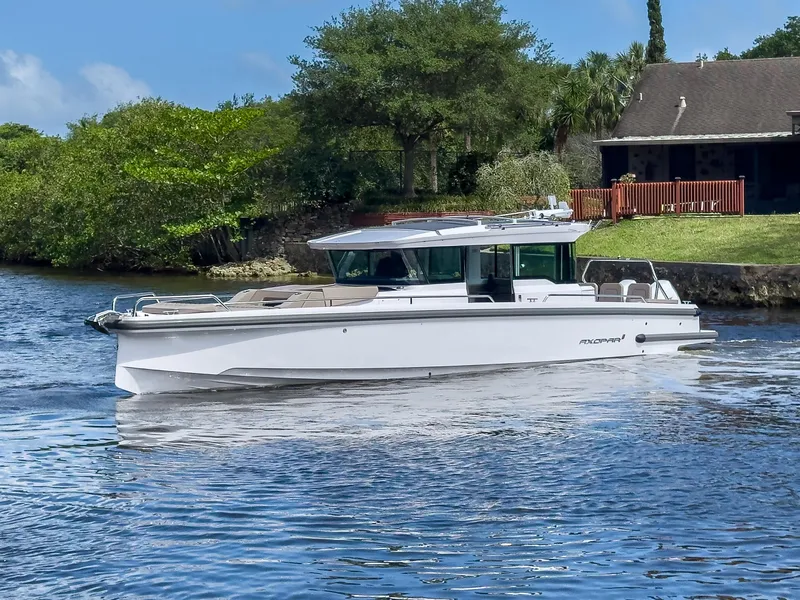 Slide: The Image of 2024 Axopar 37XC CROSS CABIN boat cruising on a serene waterway near a house. - 38