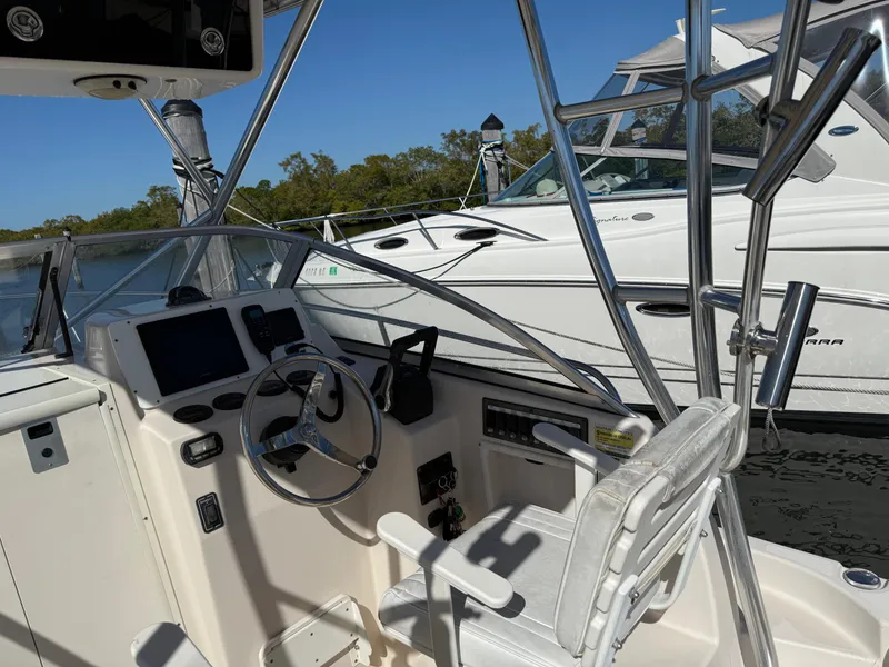 Slide: The Image of 2006 Cobia 250 Walk-Around boat cockpit with steering wheel and controls, docked beside another boat. - 8