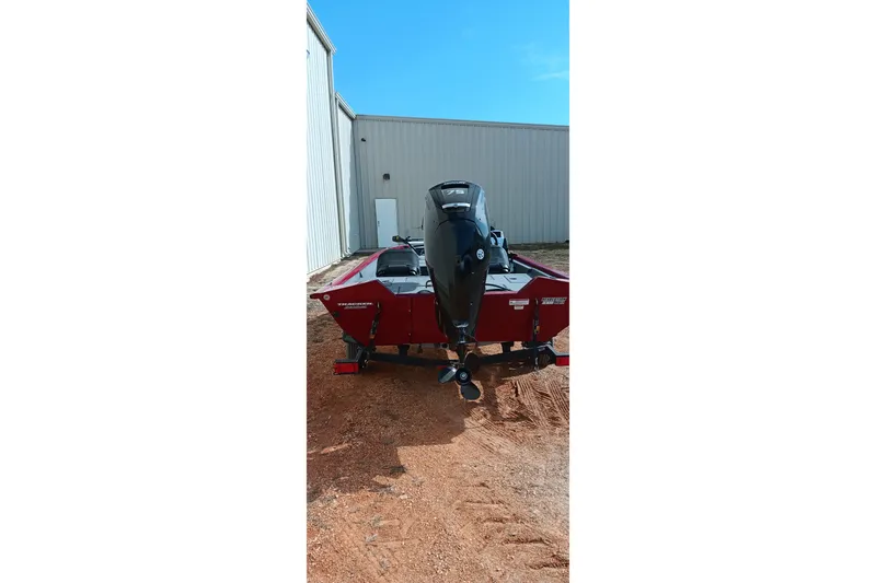 Slide: The Image of 2025 Tracker Pro Team 175 boat with outboard motor, parked near a building. - 15