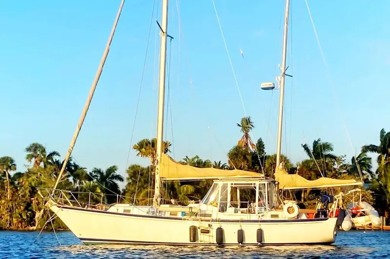 Slide: The Image of 1975 Whitby 42 Ketch sailboat anchored near palm trees under a clear blue sky. - 1
