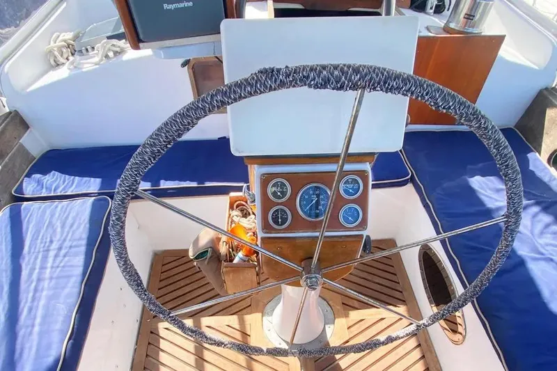 Slide: The Image of Steering wheel of a 1975 Whitby 42 Ketch sailboat with blue seating and wooden flooring. - 2
