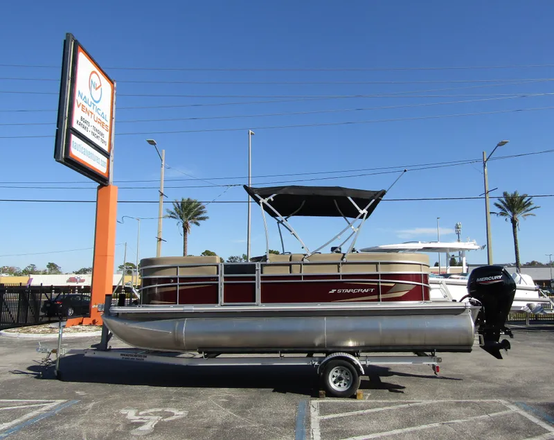 Slide: The Image of 2024 Starcraft LX 20 R pontoon boat on trailer in sunny parking lot. - 0