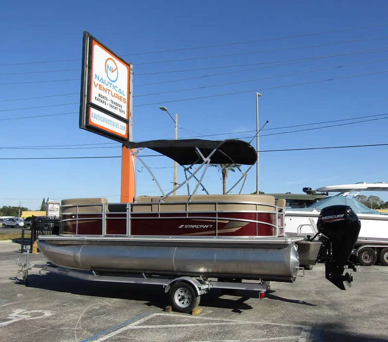 Slide: The Image of 2024 Starcraft LX 20 R pontoon boat on trailer at Nautical Ventures dealership. - 1
