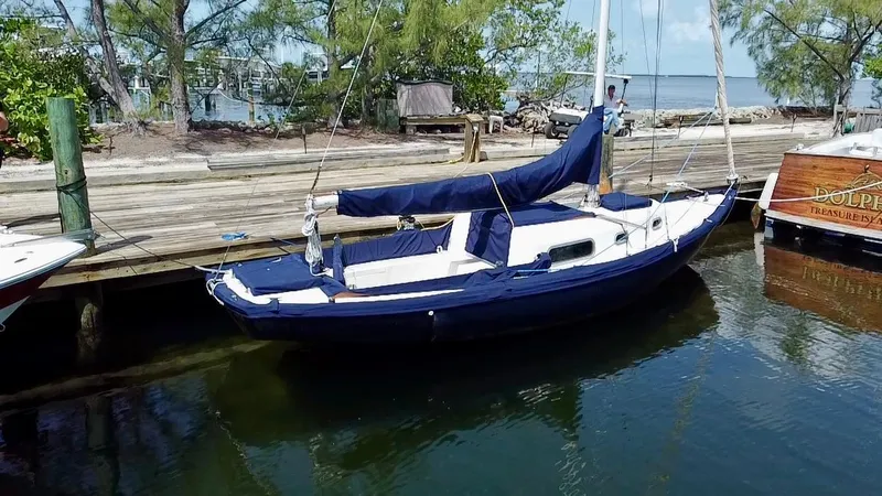 Slide: The Image of Vintage 1968 Sailboat 24 docked by a wooden pier, surrounded by trees and calm water. - 2