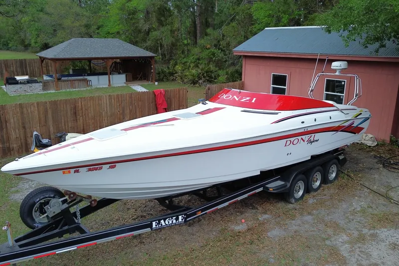 The Image of 1998 Donzi 33 ZX speedboat on trailer, parked near a wooden fence and gazebo. - 0