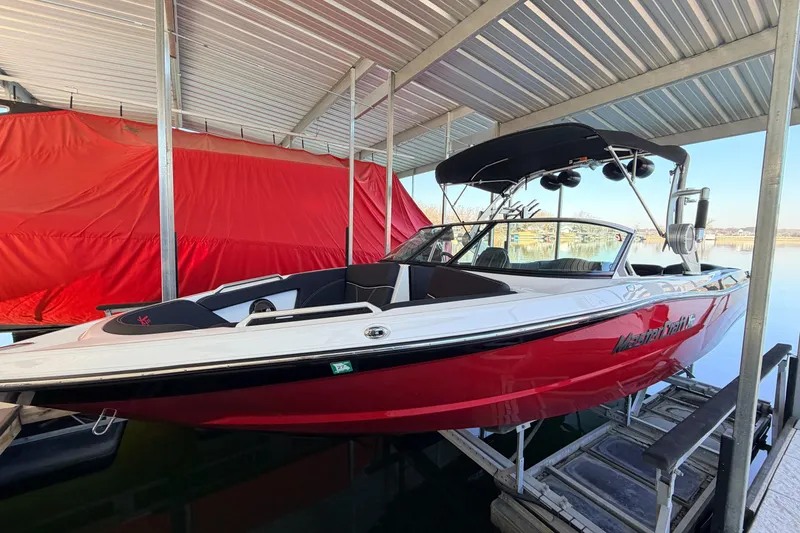 Slide: The Image of 2020 MasterCraft XT25 boat in dock, red and white exterior, under metal canopy. - 2