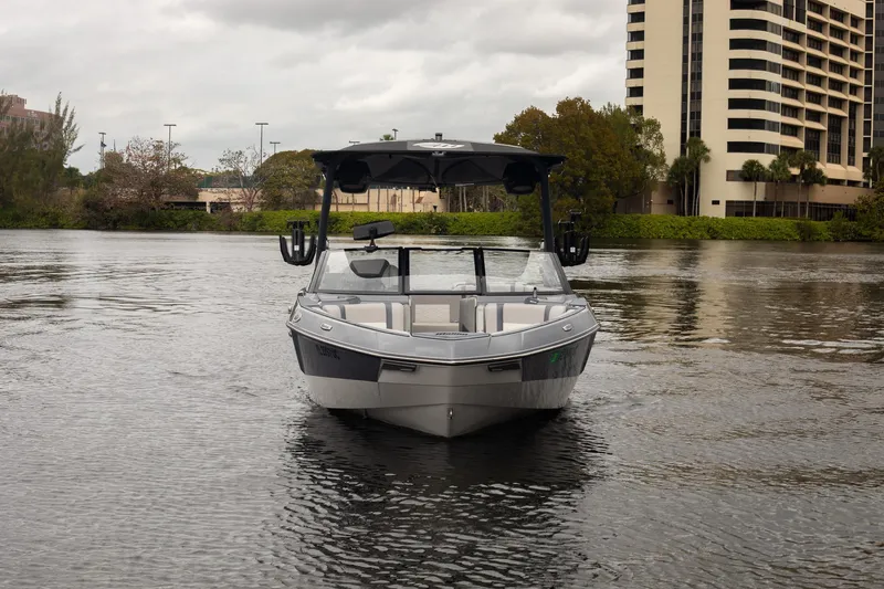 Slide: The Image of 2026 Malibu Wakesetter 23 LSV boat on a calm river near urban buildings. - 2
