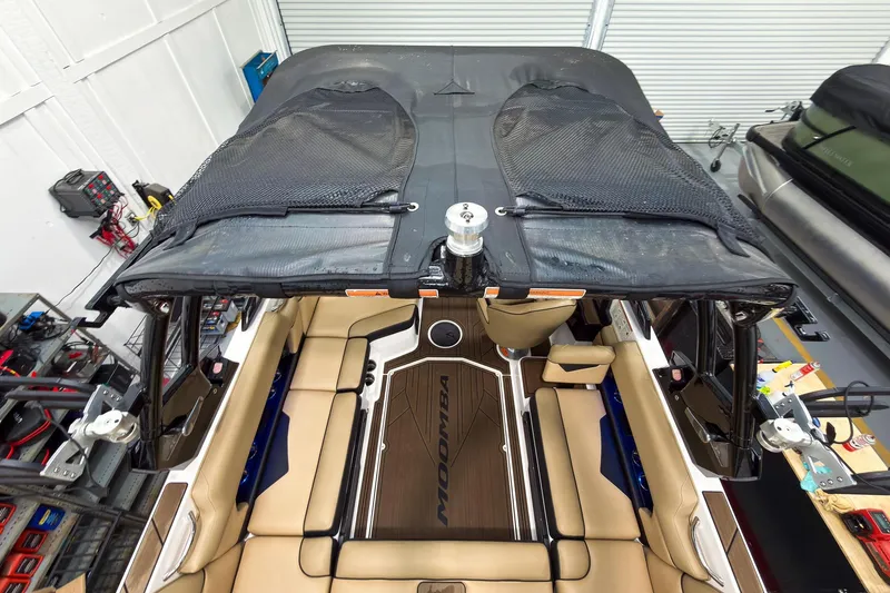 Slide: The Image of 2020 Moomba Kaiyen boat interior with tan seating and black canopy in a garage setting. - 15