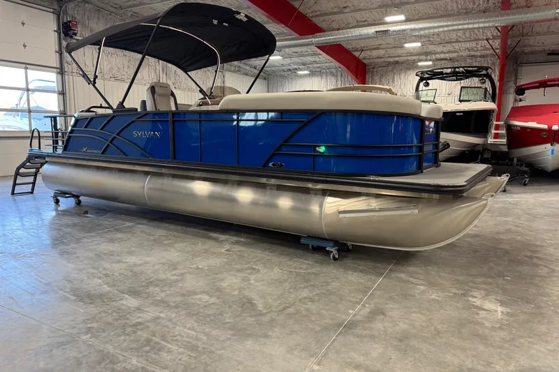 The Image of 2026 Sylvan X 5 pontoon boat in showroom, featuring sleek blue design and canopy. - 1