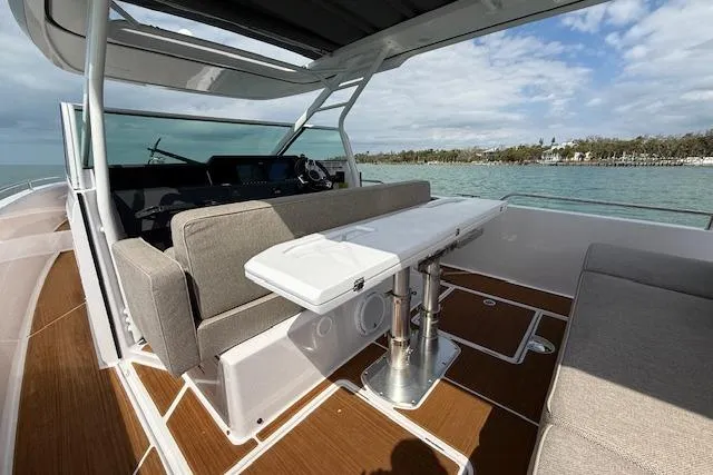 Slide: The Image of 2024 Axopar 37 Sun-Top boat interior with seating and table, overlooking serene waters. - 8