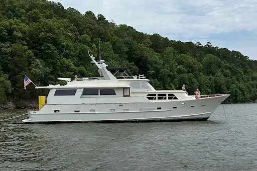 Slide: The Image of 1984 Broward CPMY Raised Pilothouse yacht on a serene lake with lush green forest backdrop. - 4