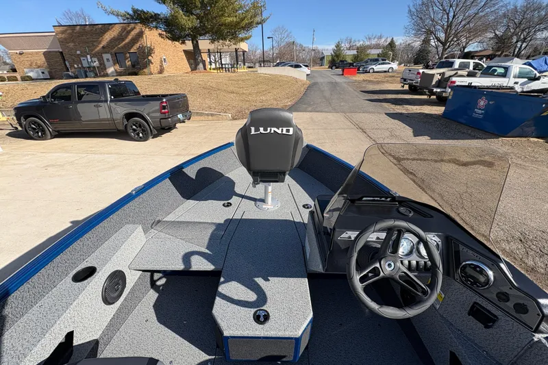 Slide: The Image of 2026 Lund 1775 Adventure SS boat interior with steering wheel and seating, parked outdoors. - 15