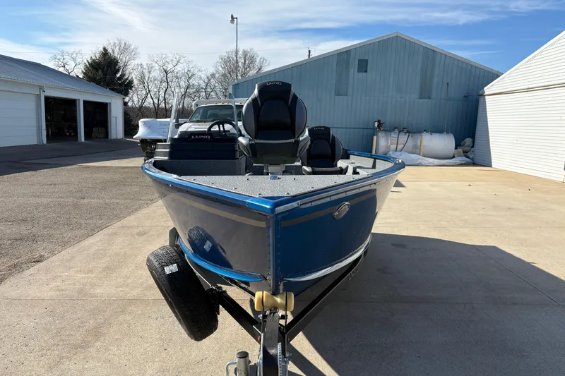 Slide: The Image of 2026 Lund 1775 Adventure SS boat in driveway, blue exterior, parked near garages. - 6