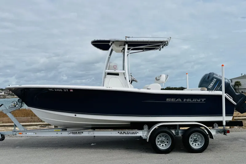 Slide: The Image of 2012 Sea Hunt Ultra 211 boat on trailer, parked near coastal area under cloudy sky. - 6