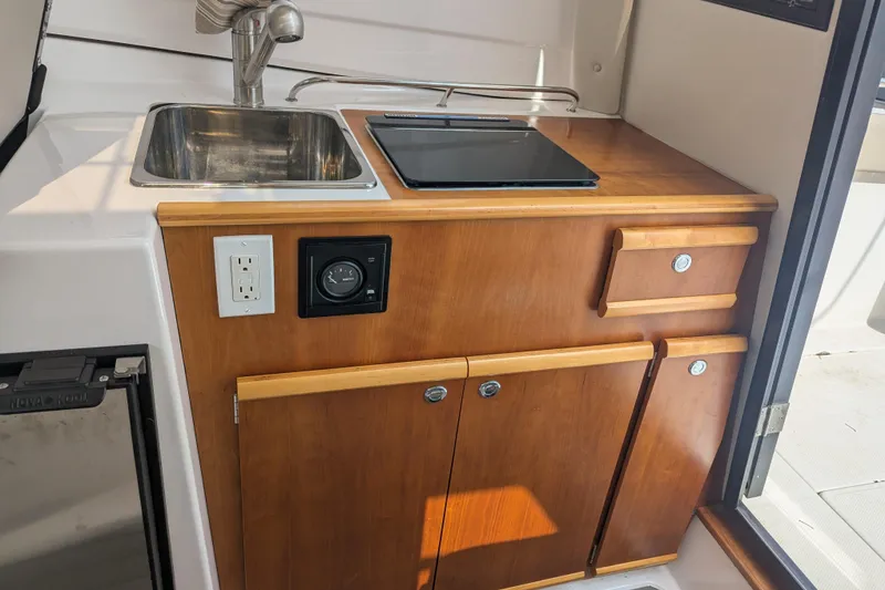 Slide: The Image of 2020 Cutwater C-24 Coupe interior kitchenette with sink, stove, and wooden cabinetry. - 5