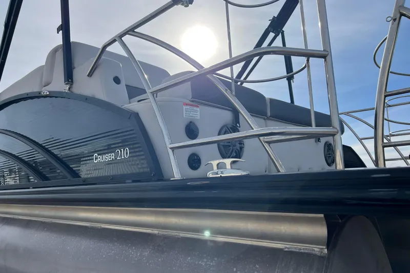 Slide: The Image of 2023 Harris Cruiser 210 SL pontoon boat under bright sun, showcasing sleek design and railing. - 15