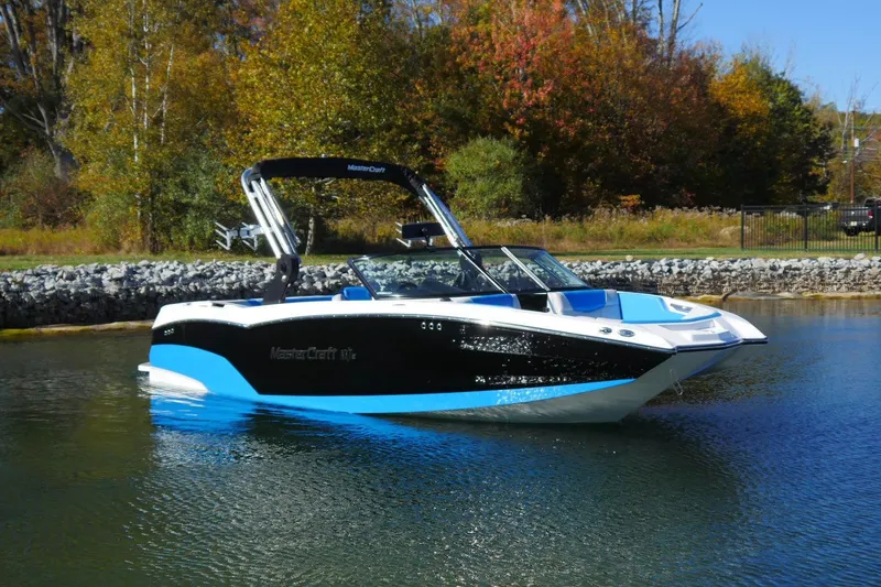 The Image of 2020 MasterCraft NXT22 boat on a calm lake with autumn trees in the background. - 1