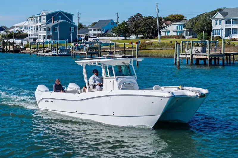 The Image of 2026 World Cat 325 CC cruising on a scenic waterfront with houses in the background. - 1