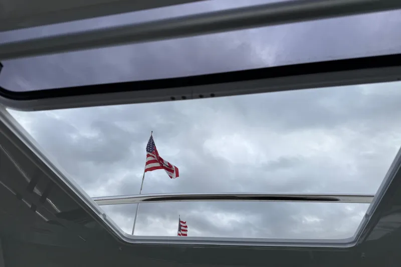 Slide: The Image of View through Jeanneau NC 695 Sport 2024 sunroof, American flag against cloudy sky. - 18