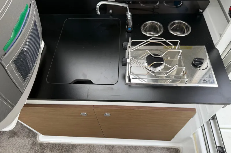 Slide: The Image of 2024 Jeanneau NC 695 Sport boat kitchen with stove, sink, and storage. - 19
