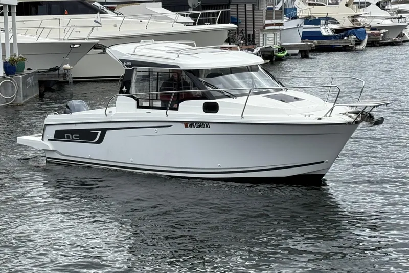 Slide: The Image of 2024 Jeanneau NC 695 Sport boat docked in a marina, showcasing sleek design and modern features. - 2