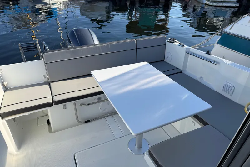 Slide: The Image of 2024 Jeanneau NC 695 Sport boat interior with seating and table, docked by water. - 32