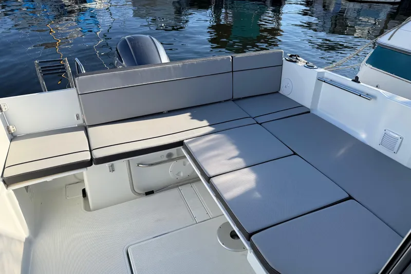Slide: The Image of 2024 Jeanneau NC 695 Sport boat interior with cushioned seating, docked on calm water. - 33
