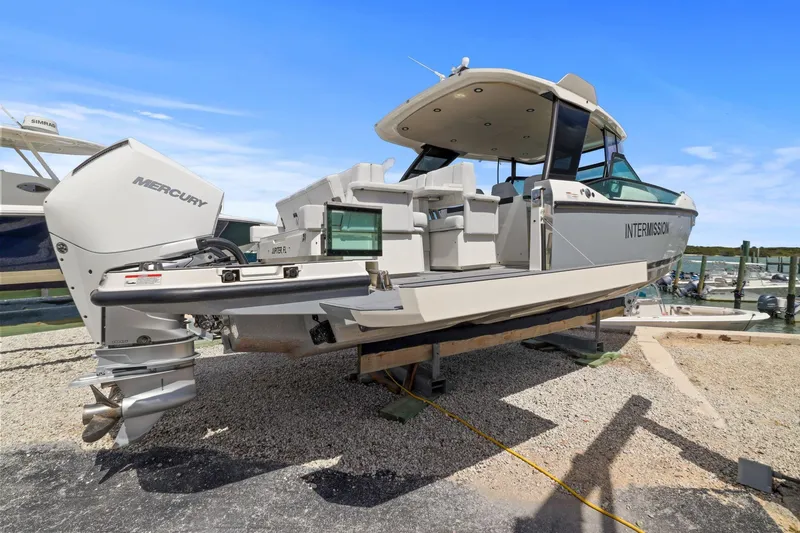 Slide: The Image of 2025 Saxdor 320 GTO boat with Mercury engine, docked on gravel, under clear blue sky. - 5