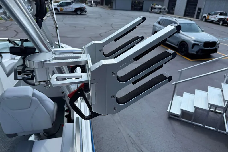 Slide: The Image of 2020 MasterCraft XT23 boat with wakeboard rack, parked in a lot with vehicles. - 19