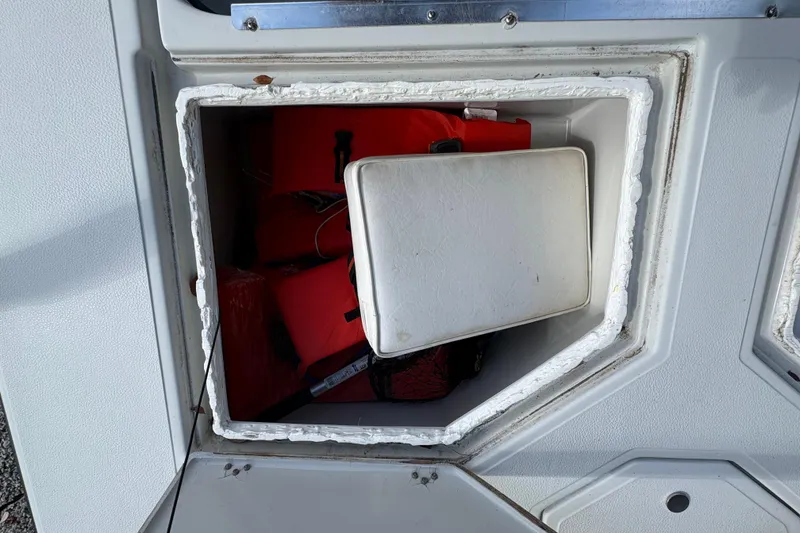 Slide: The Image of Storage compartment on a 1994 Hewes Redfisher 18 boat, containing red life jackets. - 14