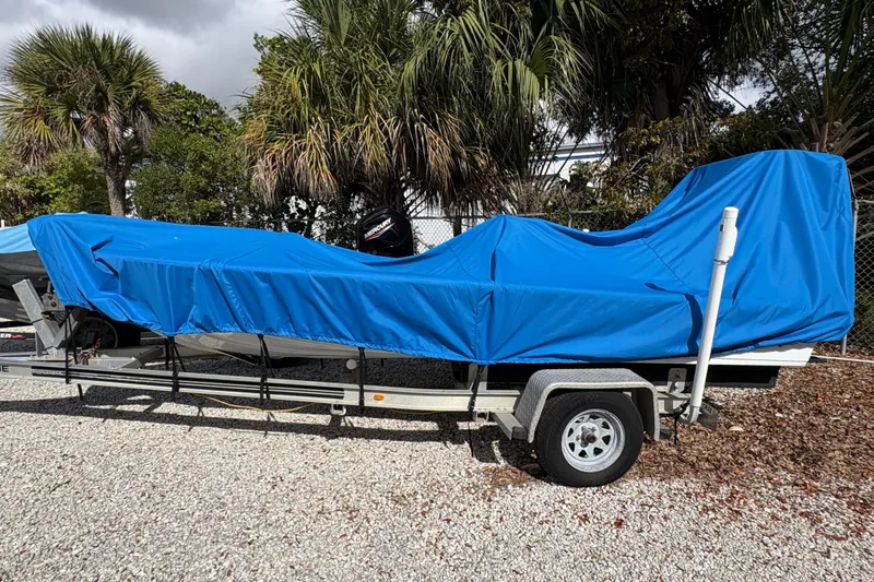 Slide: The Image of 1994 Hewes Redfisher 18 boat covered in blue tarp on trailer, surrounded by palm trees. - 5