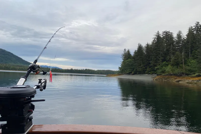 Slide: The Image of Fishing rod on Kadey-Krogen 42 boat, serene lake, forested shoreline, overcast sky, 1986 model. - 50