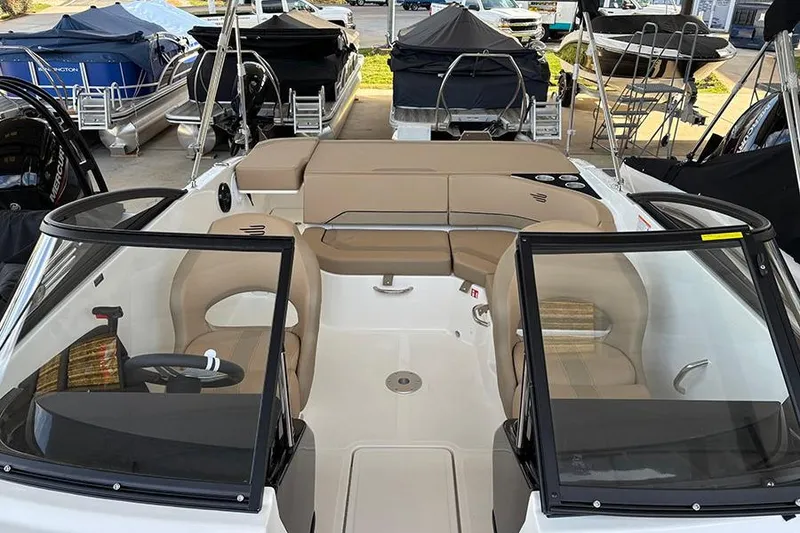 Slide: The Image of 2026 Bayliner V20i boat interior with beige seating and black windshields in a showroom. - 26