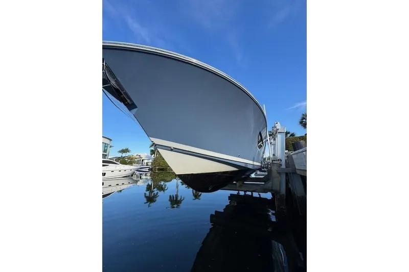 Slide: The Image of 2023 Pursuit S 428 Sport boat docked, reflecting on calm water under a clear blue sky. - 17