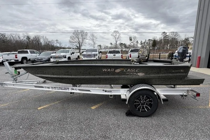 Slide: The Image of 2026 War Eagle 750 Gladiator boat on trailer, parked in lot with trucks. - 12