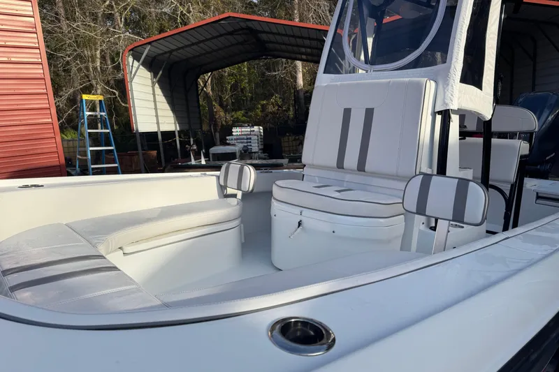 Slide: The Image of 2023 Contender 25 Bay boat interior with cushioned seating and storage, parked under a metal shelter. - 17