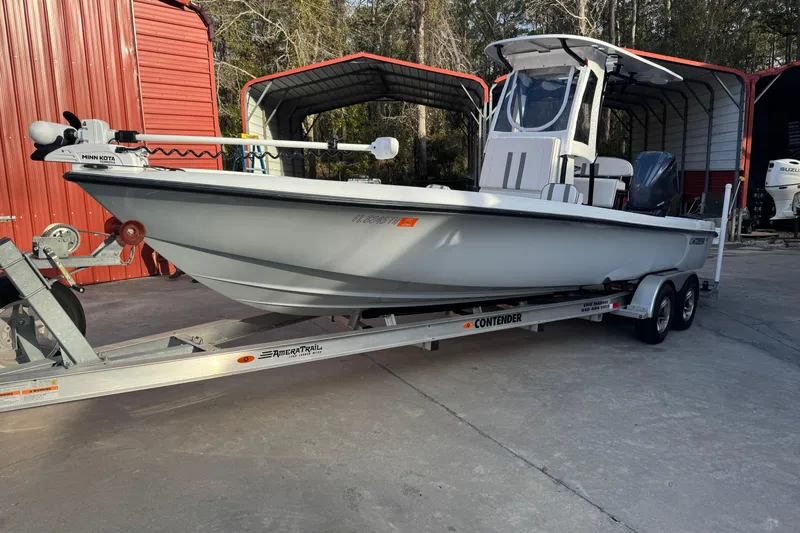 Slide: The Image of 2023 Contender 25 Bay boat on trailer, parked near red storage building. - 4