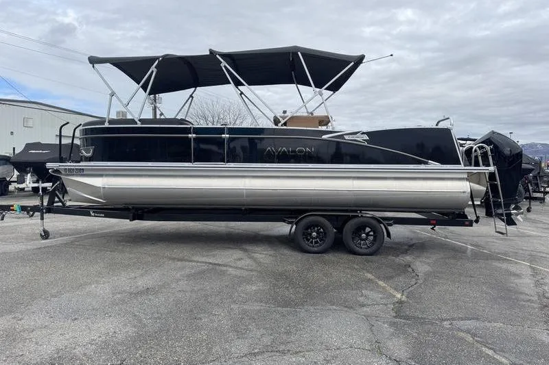 The Image of 2025 Avalon 2585 25 Catalina ENT pontoon boat on trailer, black canopy, parked outdoors. - 1