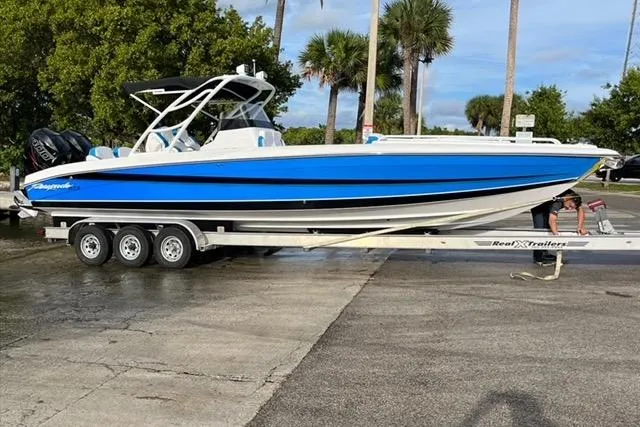 The Image of 2023 Renegade 32' Cuddy boat on trailer, vibrant blue and white design, parked outdoors. - 1