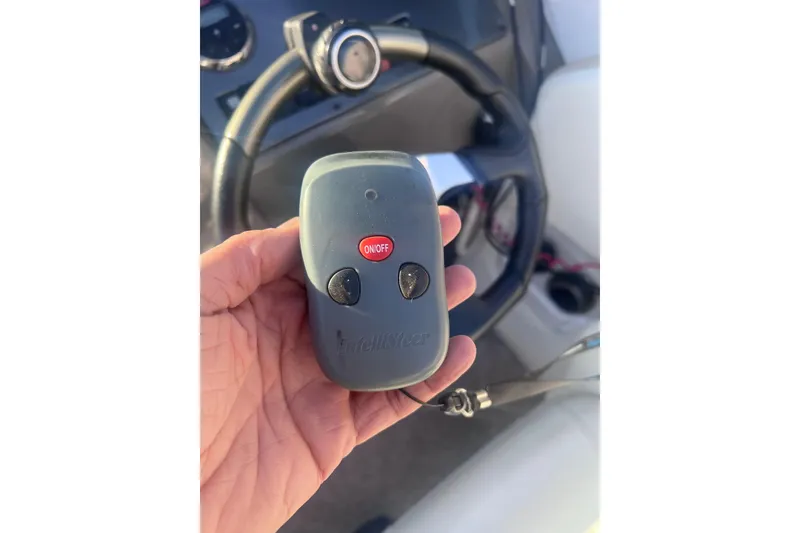 Slide: The Image of Hand holding a remote control in a 2007 Rinker 230 Captiva Atlantic boat cockpit. - 22