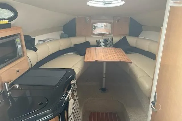 Slide: The Image of 2013 Glastron GS 289 boat interior with cozy seating, table, and kitchenette. - 6