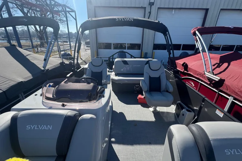 Slide: The Image of 2025 Sylvan L3 DLZ pontoon boat interior with seating and helm, docked outdoors. - 5