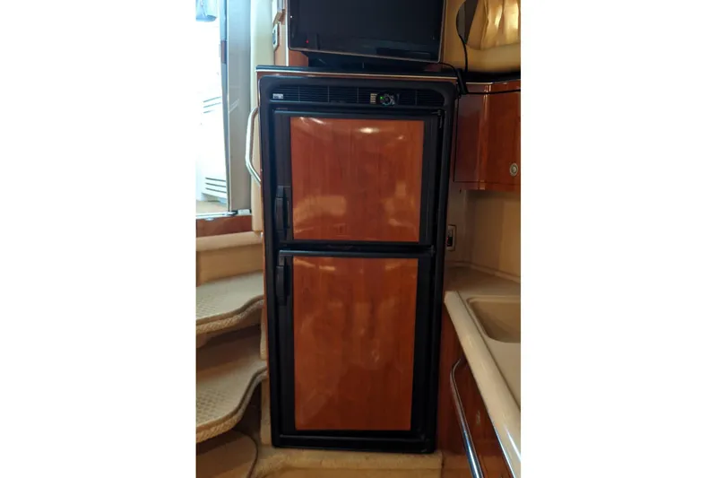 Slide: The Image of 2004 Sea Ray 380 Sundancer interior with wooden-paneled refrigerator and compact kitchen area. - 18