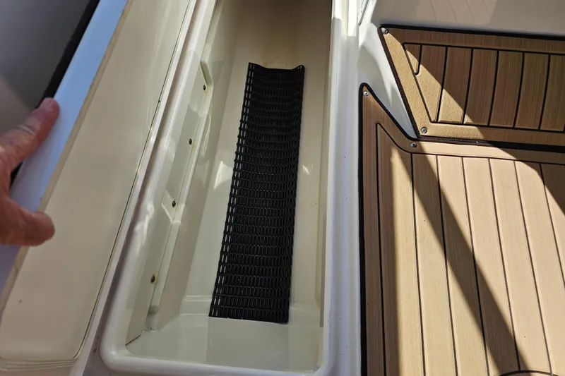 Slide: The Image of 2022 Yamaha Boats 252SD storage compartment with non-slip mat and wooden deck. - 27