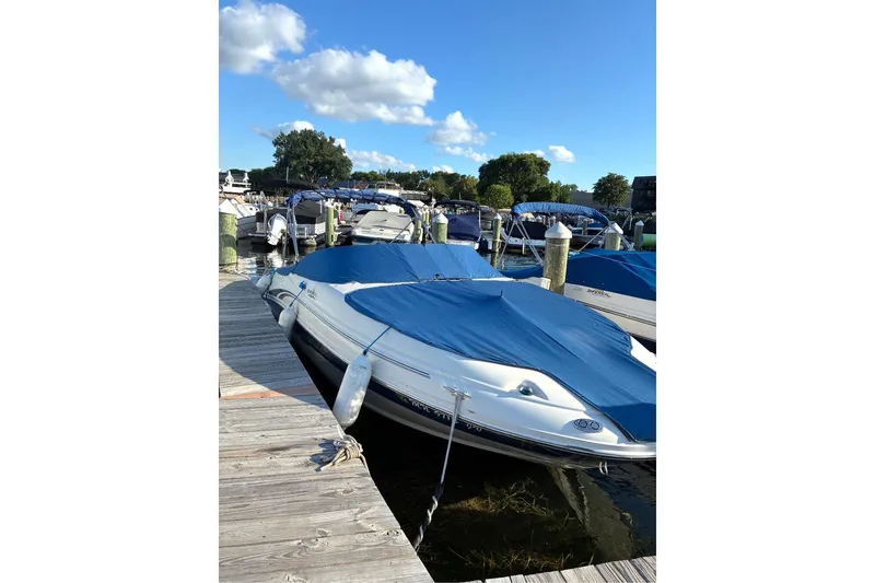Slide: The Image of 2004 Sea Ray 220 Sundeck boat docked with blue cover, clear sky background. - 2