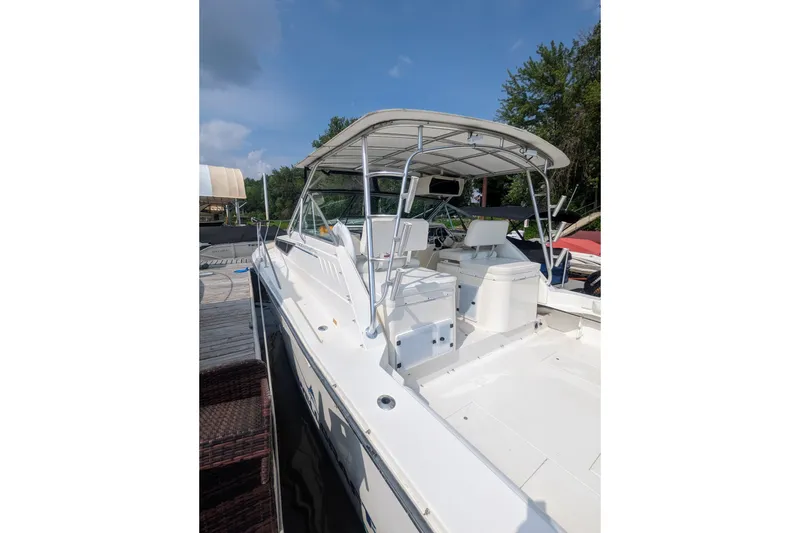 Slide: The Image of 1995 Wellcraft 330 Coastal boat docked, featuring spacious deck and canopy under clear skies. - 26