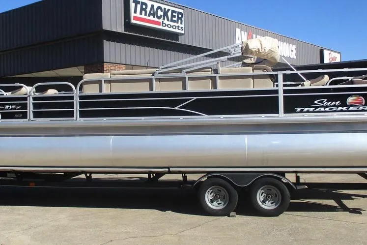 The Image of 2026 Sun Tracker Fishin' Barge 24 DLX pontoon boat on trailer at dealership. - 0