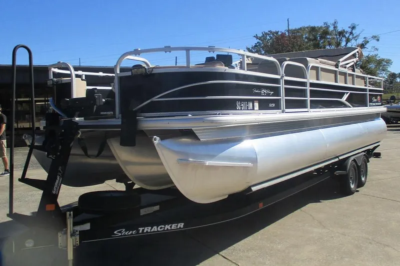 Slide: The Image of 2026 Sun Tracker Fishin' Barge 24 DLX pontoon boat on trailer, outdoor setting. - 2